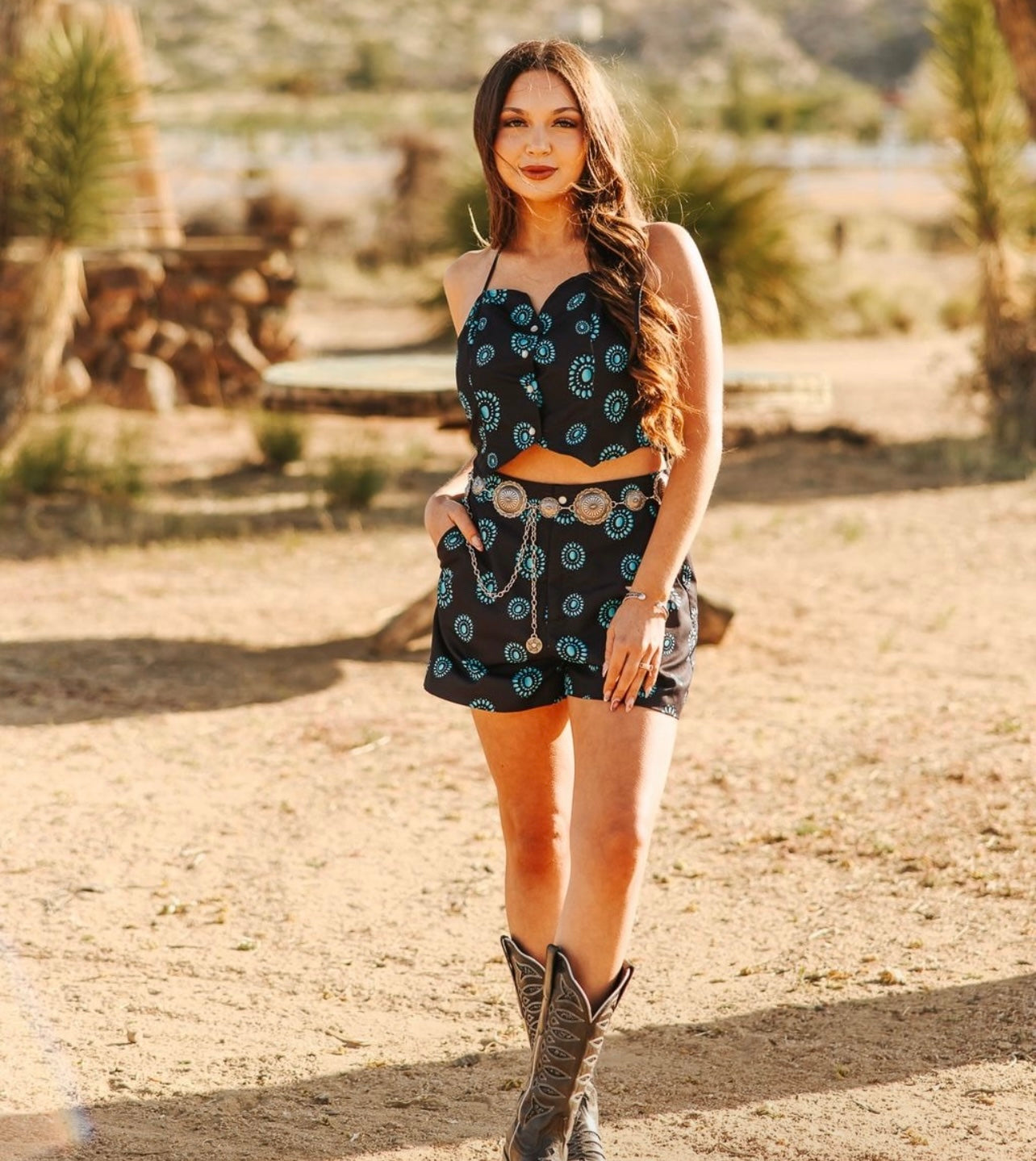 Woman in a black concho patterned outfit with cowboy boots standing in a desert-like setting