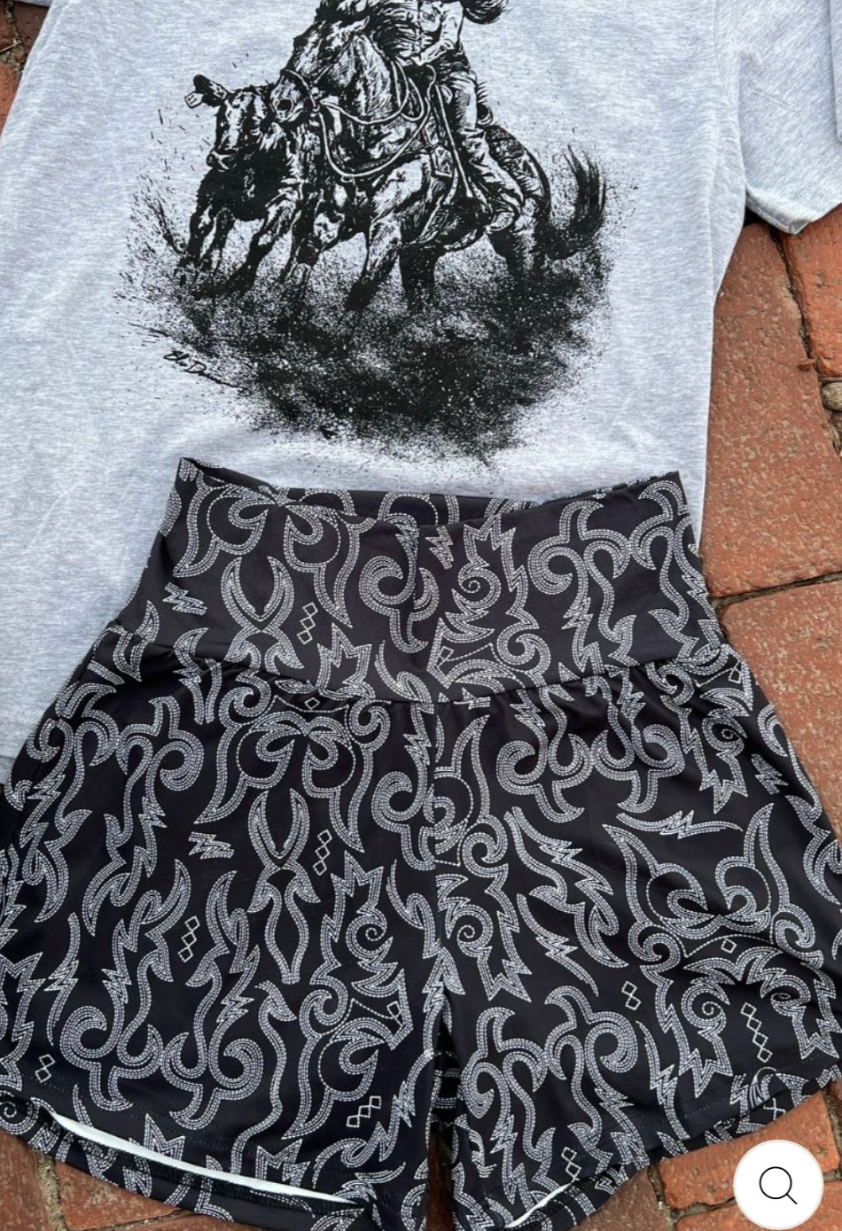 Gray t-shirt with a graphic of a person on horseback and black shorts with white patterns on a tiled floor.