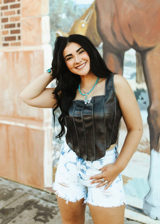 Woman wearing a leather top and denim shorts standing in front of a mural.