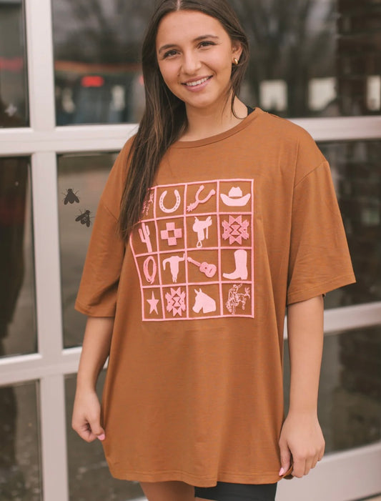 Woman wearing a brown t-shirt with pink graphics in front of a window.