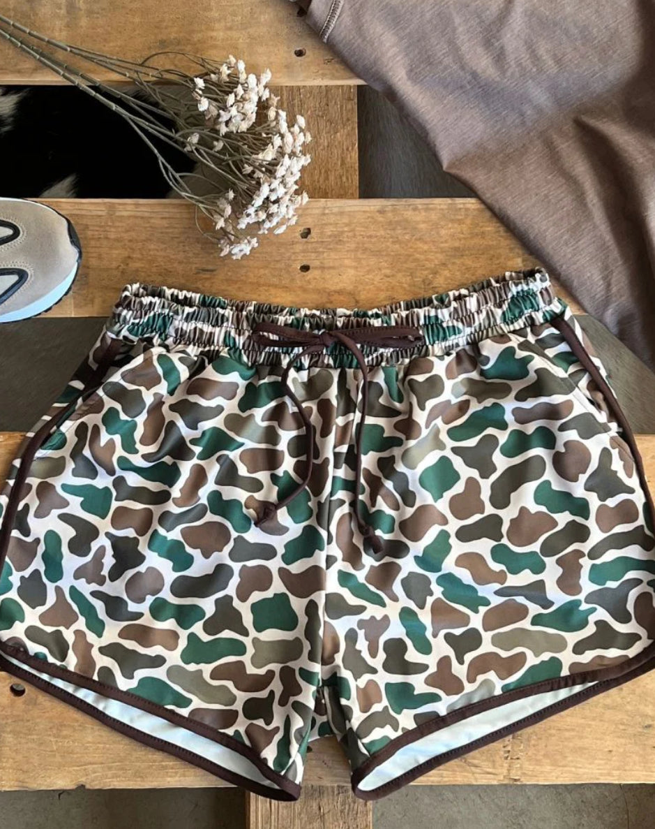 Camouflage-patterned shorts on a wooden surface with dried flowers.