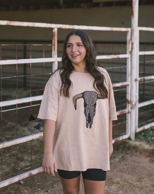 Woman wearing a beige t-shirt with a graphic design in front of a metal gate.